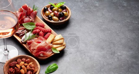 Photo for Antipasto board with prosciutto, salami, crackers, cheese, nuts, olives and rose wine. With copy space - Royalty Free Image