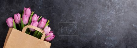 Foto de Flores de tulipán rosadas frescas en bolsa de papel sobre mesa de piedra oscura. Vista superior plano con espacio de copia - Imagen libre de derechos