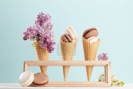 Foto de Varias galletas de macarrones en conos de helado y flores lila - Imagen libre de derechos