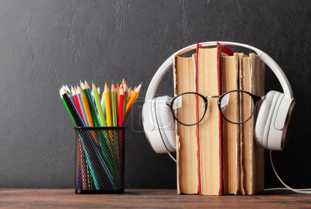 Photo for Old books, headphones and eyeglasses on wooden table and blackboard for copy space. Audiobooks and education template - Royalty Free Image