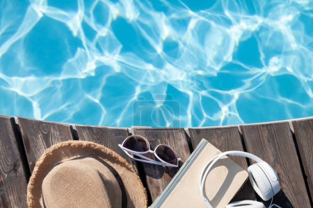 Téléchargez les photos : Livre et écouteurs près de la piscine. Vacances d'été. Pose plate avec espace de copie - en image libre de droit