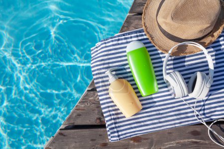 Téléchargez les photos : Bouteilles cosmétiques, écouteurs et chapeau de soleil près de la piscine. Vacances d'été. Pose plate avec espace de copie - en image libre de droit