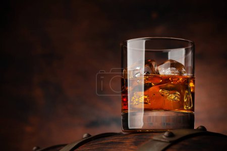 Foto de Un vaso de whisky con cubitos de hielo en el viejo barril. Con espacio de copia sobre fondo de madera - Imagen libre de derechos