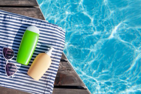 Téléchargez les photos : Bouteilles cosmétiques et lunettes de soleil près de la piscine. Vacances d'été. Pose plate avec espace de copie - en image libre de droit