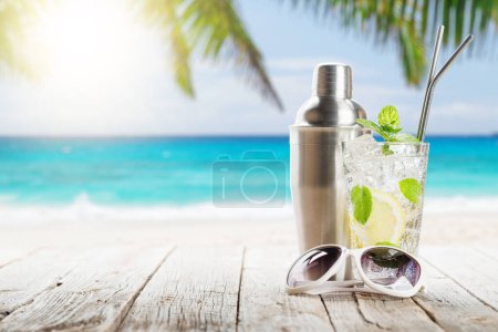 Photo for Mojito cocktail on wooden table in front of sunny sea and palm leaves - Royalty Free Image