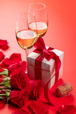 Foto de Tarjeta de San Valentín con champán, flores de rosas y caja de regalo. Sobre fondo rojo con espacio para tus saludos - Imagen libre de derechos