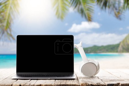 Foto de Laptop and headphones on wooden table in front of sunny sea and palm leaves. Work and travel or remote business concept - Imagen libre de derechos