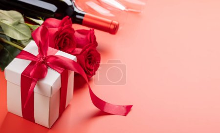 Téléchargez les photos : Carte Saint Valentin avec vin, fleurs roses et coffret cadeau. Sur fond rouge avec espace pour vos salutations - en image libre de droit