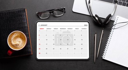 Foto de Tableta con aplicación de calendario, taza de café y suministros de oficina en el escritorio. Vista superior plano laico - Imagen libre de derechos
