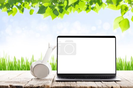 Téléchargez les photos : Laptop with blank screen and headphones on wooden table in front of sunny landscape. Work and travel or remote business concept - en image libre de droit