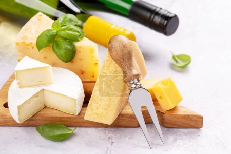 Photo for Various cheese on board and white wine bottles - Royalty Free Image