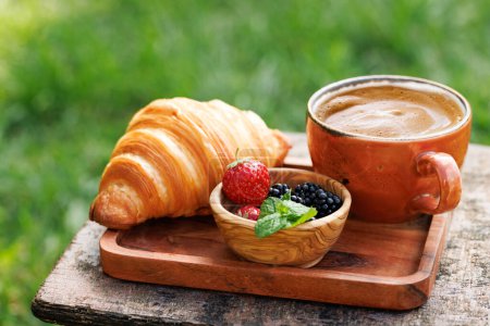 Foto de Taza de café y croissant en la mesa de jardín exterior. Comida al aire libre soleada - Imagen libre de derechos