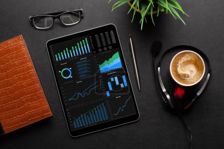 Photo for Tablet with business reports and charts, coffee cup and office supplies on desk. Top view flat lay - Royalty Free Image