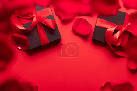 Foto de Tarjeta de San Valentín con cajas de regalo y pétalos de flor de rosa. Sobre fondo rojo con espacio para tus saludos - Imagen libre de derechos