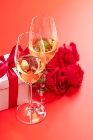 Foto de Tarjeta de San Valentín con champán, flores de rosas y caja de regalo. Sobre fondo rojo con espacio para tus saludos - Imagen libre de derechos