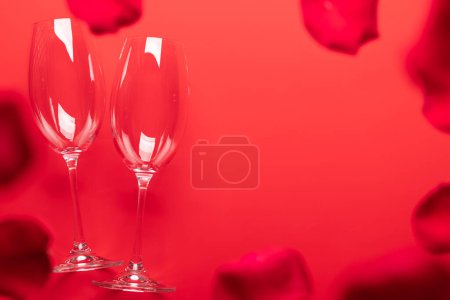 Foto de Tarjeta de San Valentín con copas de champán y pétalos de rosa. Sobre fondo rojo con espacio para tus saludos. Puesta plana - Imagen libre de derechos