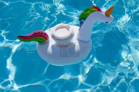 Téléchargez les photos : Drink cup in inflatable unicorn toy in swimming pool. Summer vacation and holiday concept - en image libre de droit