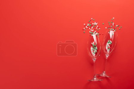 Foto de Tarjeta de San Valentín con copas de champán y dulces en forma de estrella. Sobre fondo rojo con espacio para tus saludos - Imagen libre de derechos