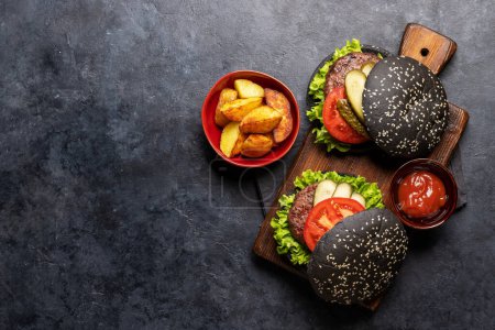 Photo for Homemade beef burgers with black buns and french fries. Flat lay with copy space - Royalty Free Image