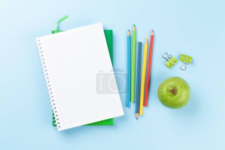 Foto de Blank notepad, apple and colorful pencils. Flat lay over blue background with copy space - Imagen libre de derechos