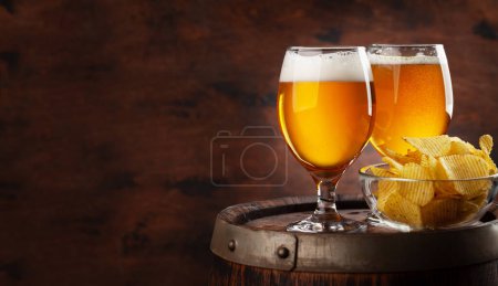 Beer glasses and potato chips on wooden barrel. With copy space