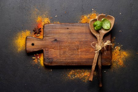 Foto de Empty cutting board over various spices on stone table. Frame with copy space for your menu or recipe - Imagen libre de derechos