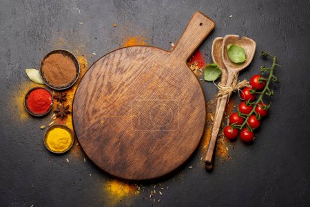 Téléchargez les photos : Empty cutting board over various spices on stone table. Frame with copy space for your menu or recipe - en image libre de droit