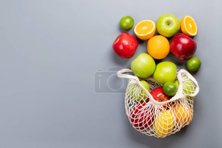 Foto de Bolsa de malla de compras llena de alimentos frutas saludables sobre fondo gris. Piso con espacio de copia - Imagen libre de derechos