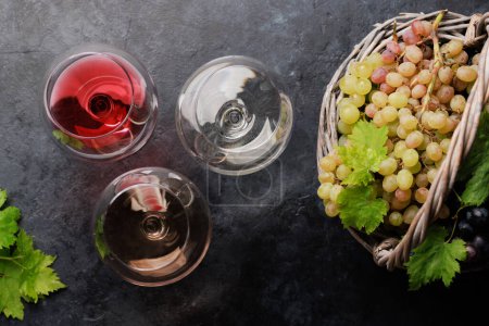 Foto de White, rose and red wine glasses and grape in basket. Flat lay - Imagen libre de derechos