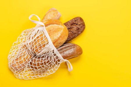 Photo for Fresh baked bread in mesh bag on yellow background. Flat lay with copy space - Royalty Free Image