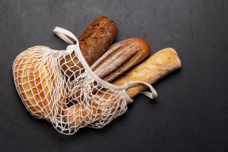 Photo for Fresh baked bread in mesh bag on stone table. Flat lay with copy space - Royalty Free Image