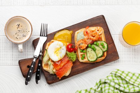 Photo for Breakfast waffles with fried eggs, salmon, bacon, cucumber and prawns. Top view flat lay with coffee, orange juice - Royalty Free Image