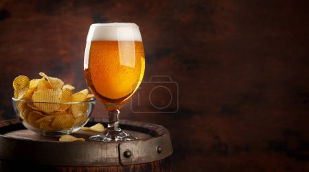 Beer glass and potato chips on wooden barrel. With copy space
