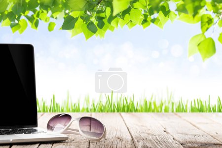 Photo for Laptop and sunglasses on wooden table in front of sunny landscape. Work and travel or remote business concept - Royalty Free Image