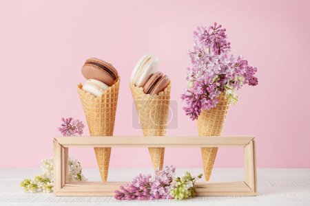 Foto de Varias galletas de macarrones en conos de helado y flores lila - Imagen libre de derechos