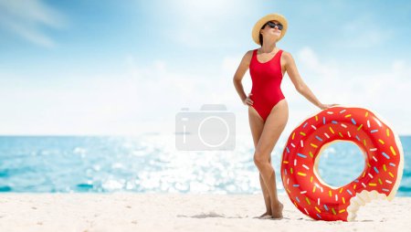 Téléchargez les photos : Beautiful young woman with inflatable donut ring relaxing on sea beach. Summer vacation. With copy space - en image libre de droit