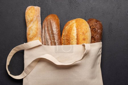 Photo for Fresh baked bread in bag on stone table. Flat lay - Royalty Free Image