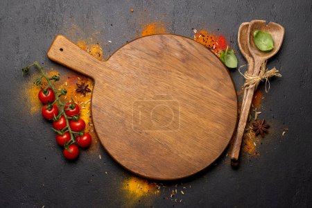 Photo for Empty cutting board over various spices on stone table. Frame with copy space for your menu or recipe - Royalty Free Image
