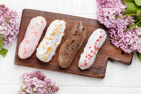 Photo for Various eclair dessert. On wooden table with lilac flowers. Top view flat lay - Royalty Free Image