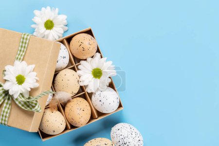 Téléchargez les photos : Gift box, Easter eggs and flowers on a blue background with space for your greetings. Flat lay - en image libre de droit