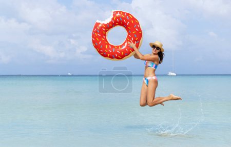 Photo for Beautiful young woman with inflatable donut ring jumping in sea. Summer vacation. With copy space - Royalty Free Image