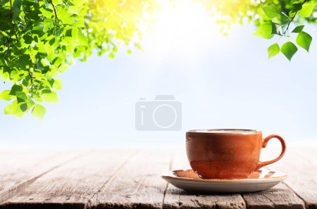 Téléchargez les photos : Tasse à café sur table en bois. Jardin extérieur ensoleillé et feuilles d'arbres - en image libre de droit