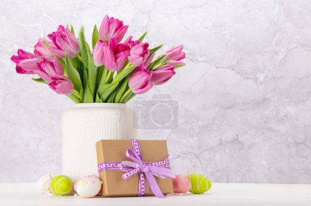 Foto de Ramo de flores de tulipán rosa fresco, huevos de Pascua y caja de regalo. En mesa de madera blanca con espacio para copiar - Imagen libre de derechos