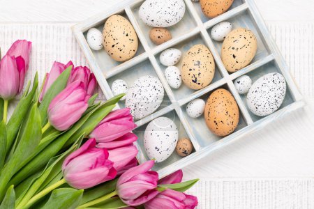 Photo for Fresh pink tulip flowers bouquet and easter eggs in wooden box. On white wooden table. Flat lay - Royalty Free Image