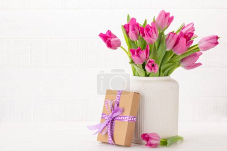 Téléchargez les photos : Bouquet de fleurs de tulipes roses fraîches et boîte cadeau. Sur table en bois blanc avec espace de copie - en image libre de droit