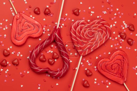 Téléchargez les photos : Various red candy sweets lollipops on red background. Valentines day candy hearts. Flat lay - en image libre de droit