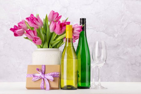 Foto de Fresh pink tulip flowers bouquet and wine. On white wooden table with copy space - Imagen libre de derechos