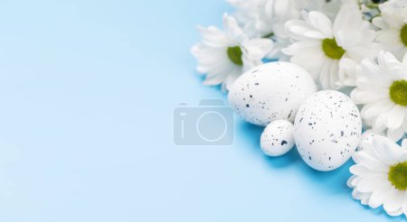 Foto de Easter eggs and flower bouquet on a blue background with space for your greetings. Flat lay - Imagen libre de derechos