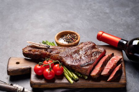 Photo for Medium rare grilled Tomahawk beef steak with asparagus and red wine. With copy space - Royalty Free Image