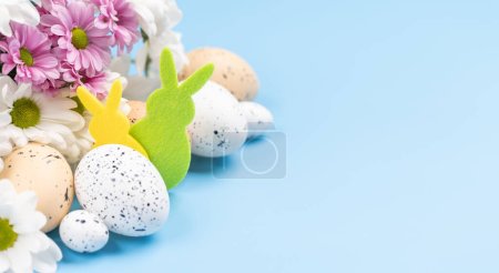 Easter eggs, rabbit decor and flower bouquet on a blue background with space for your greetings. Flat lay